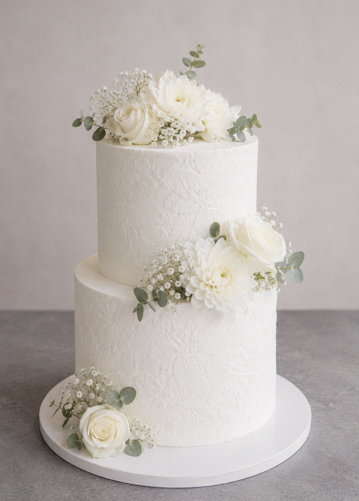 Wedding cake blanc à deux étages décoré de roses, de dahlias, de gypsophile et d’eucalyptus